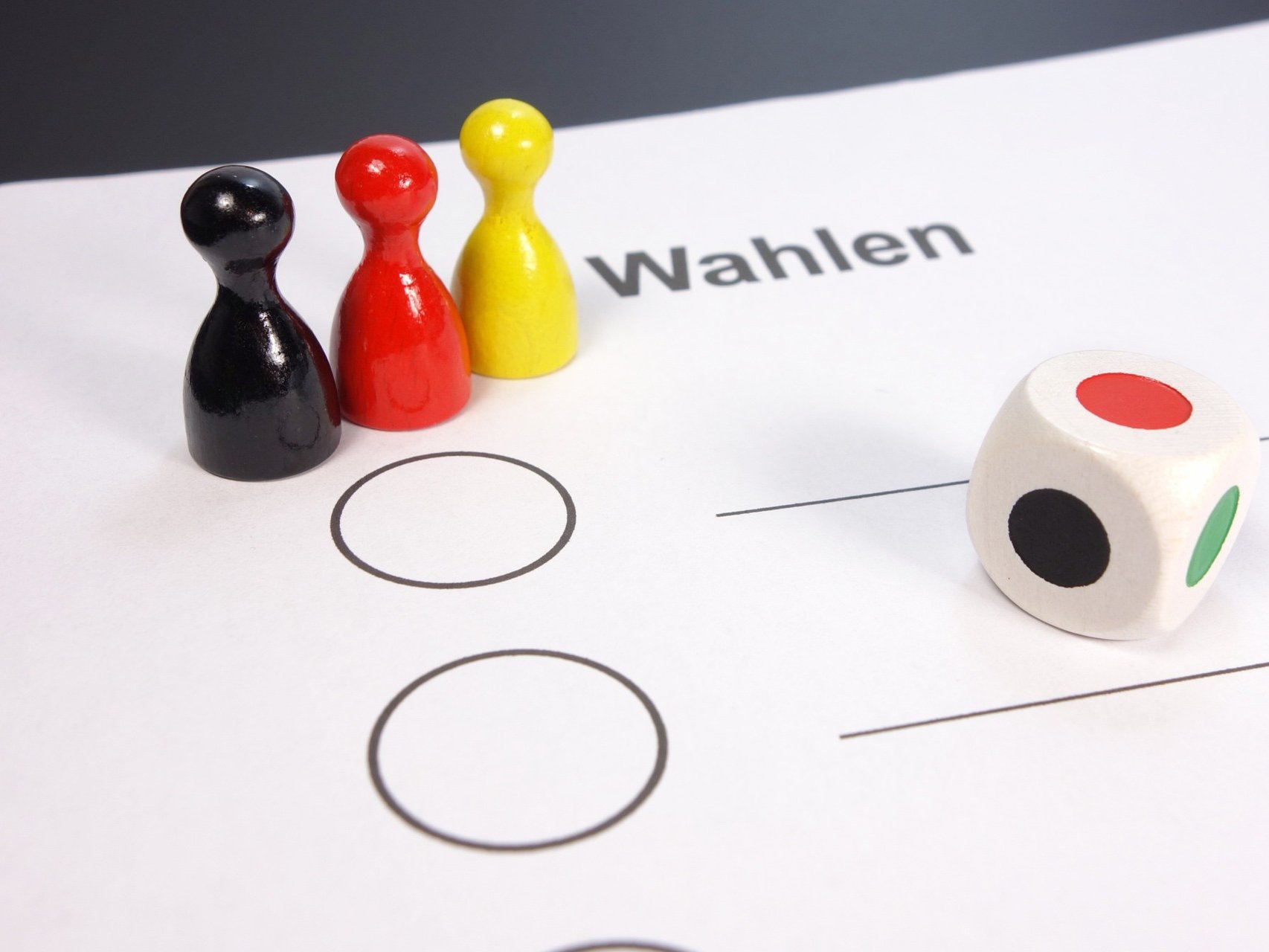 Schwarz-Rot-Goldene Spielfiguren stehen auf Wahlschein im Vordergrund ist ein Farbwürfel