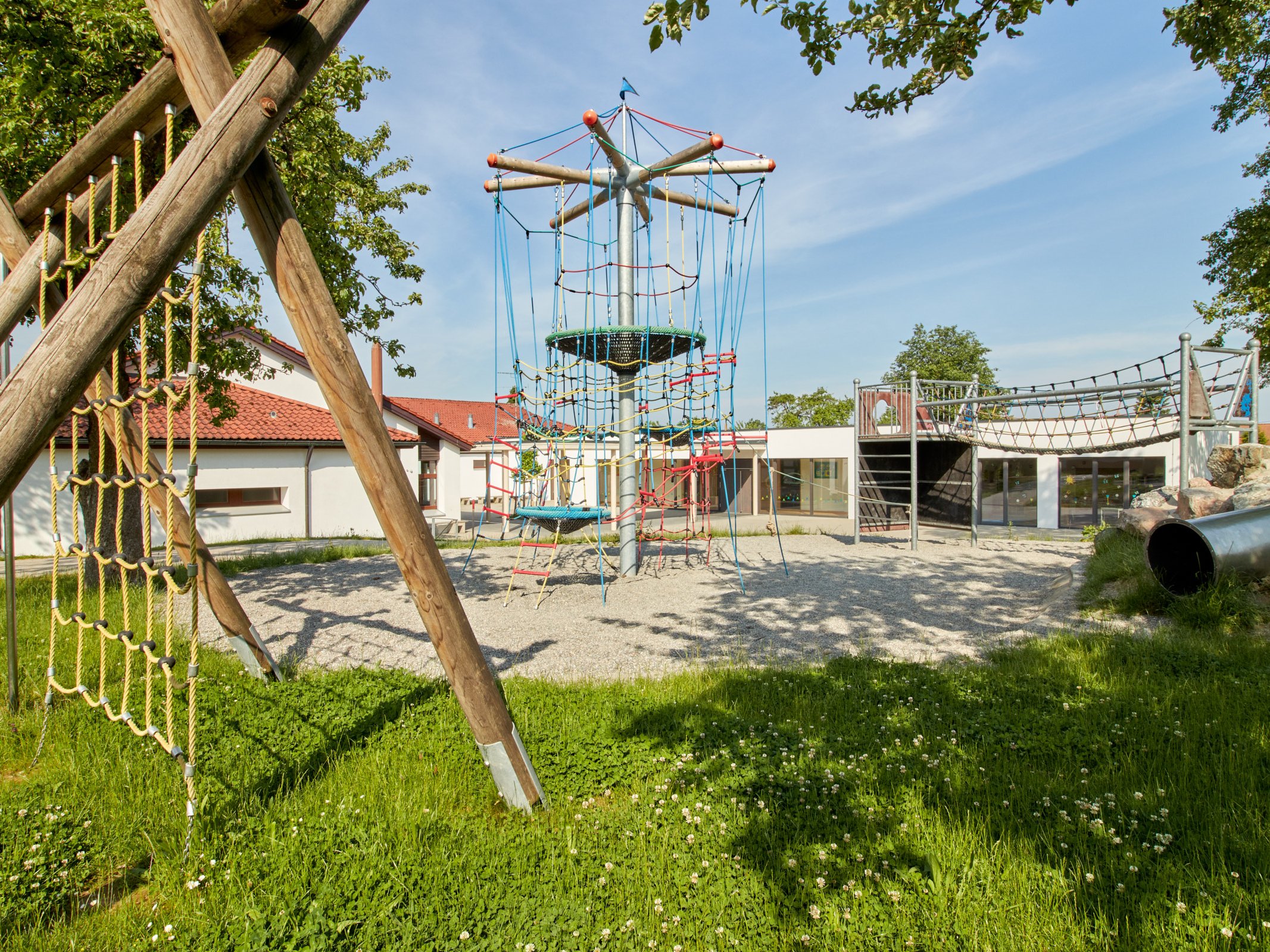 Klettergerüste unter Bäumen im Vordergrund der Grundschule