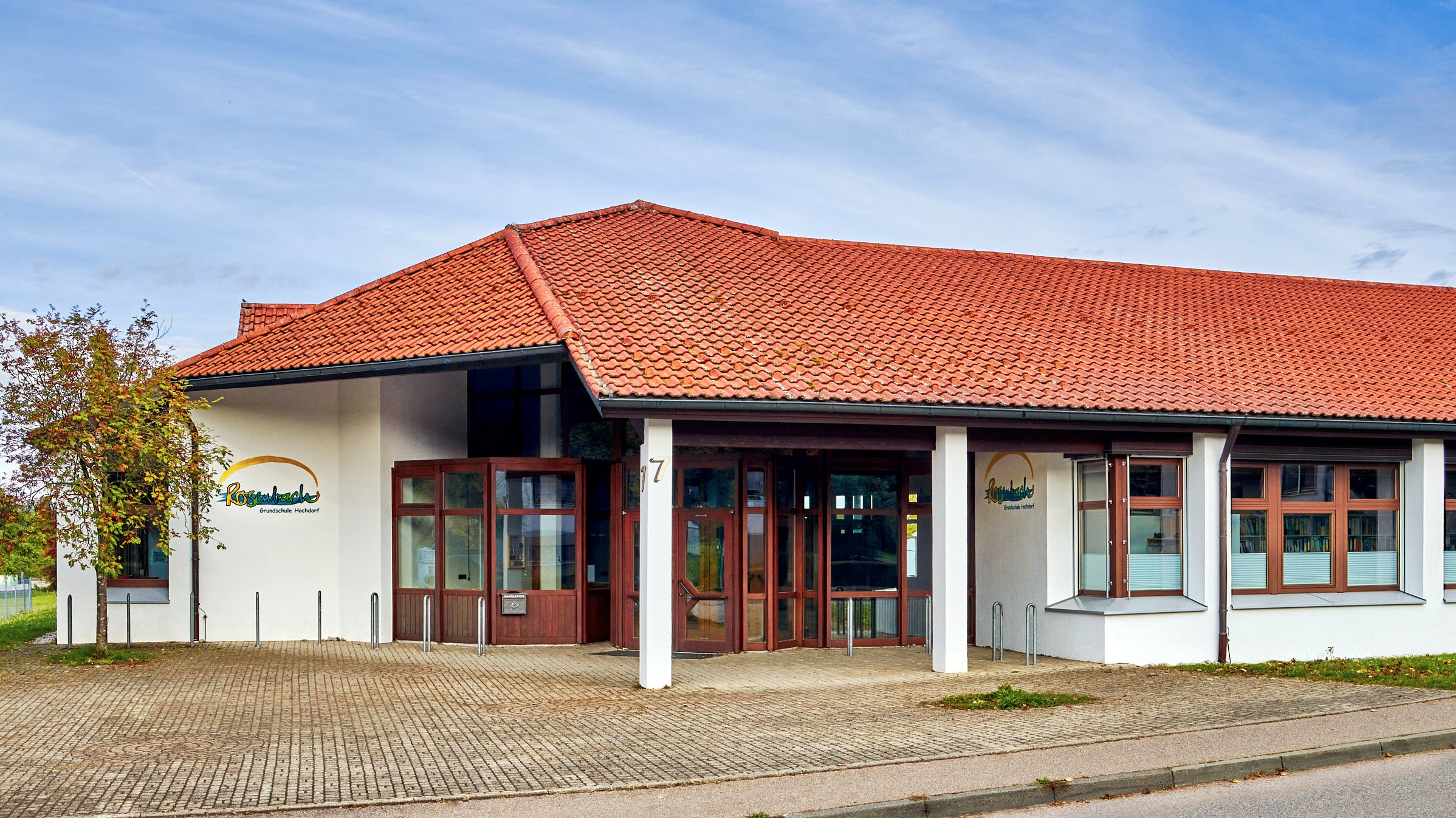 Einstöckiges Schulgebäude mit überdachtem Haupteingang vor blauem Himmel